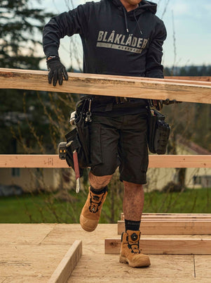 Blaklader Service Shorts with Stretch in Black and Elite Freelock Safety Boots in Wheat worn by carpenter carrying lumber