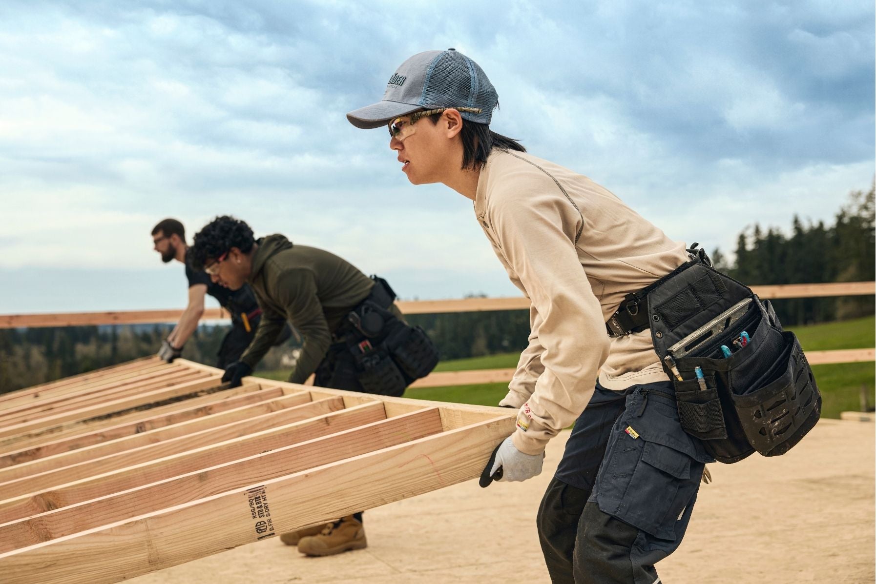 Blaklader workwear worn by male and female carpenters lifting lumber frame together on construction job site
