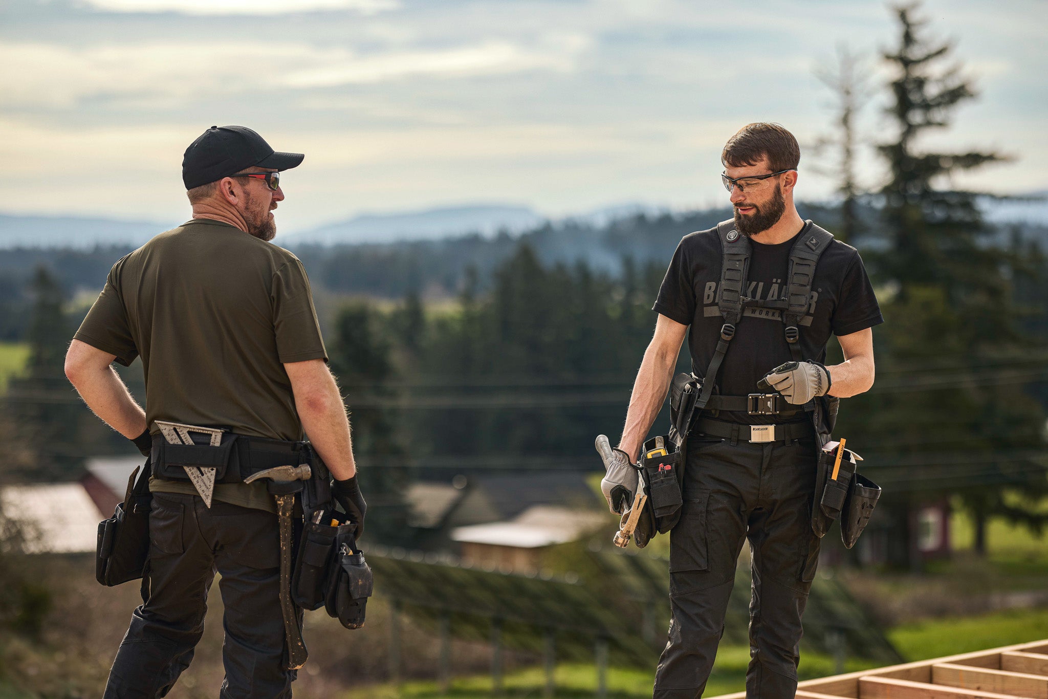 Two tradesmen in workwear attire standing outdoors with a scenic background