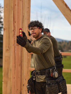 Man in workwear green sun shirt and tool belt using a level on wooden beams outdoors