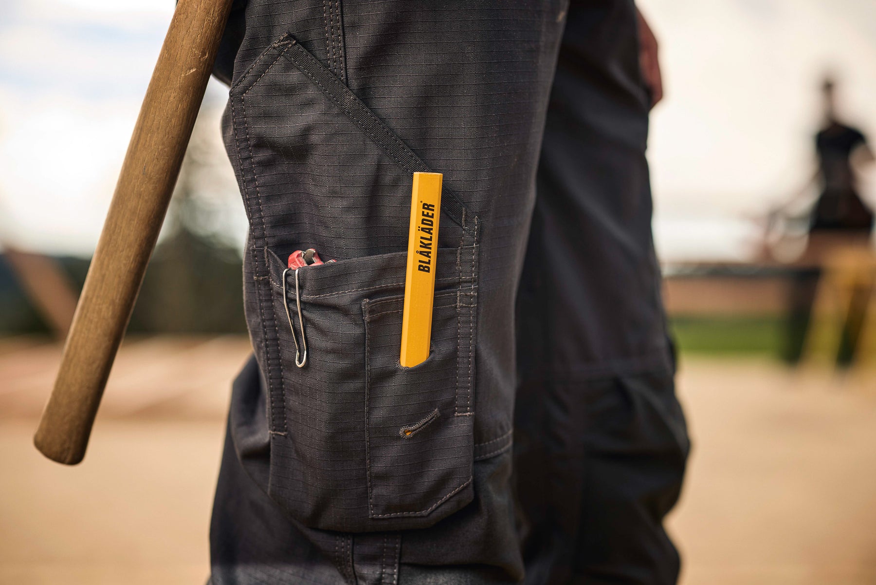 tradesman wearing dark workwear pants with a yellow label, holding a brown object.