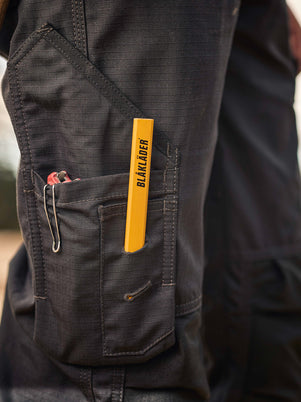tradesman wearing dark workwear pants with a yellow label, holding a brown object.