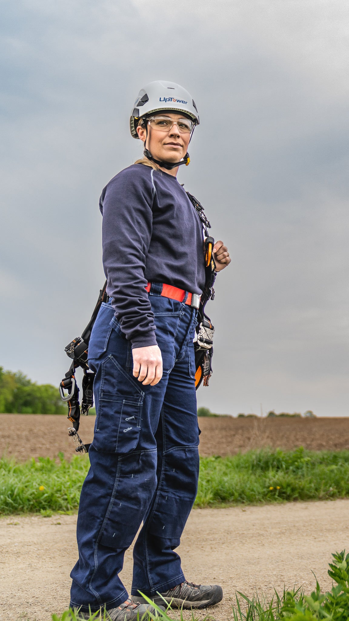 a utility tradeswoman standing near a wind turbine in flame resistant clothing - mobile