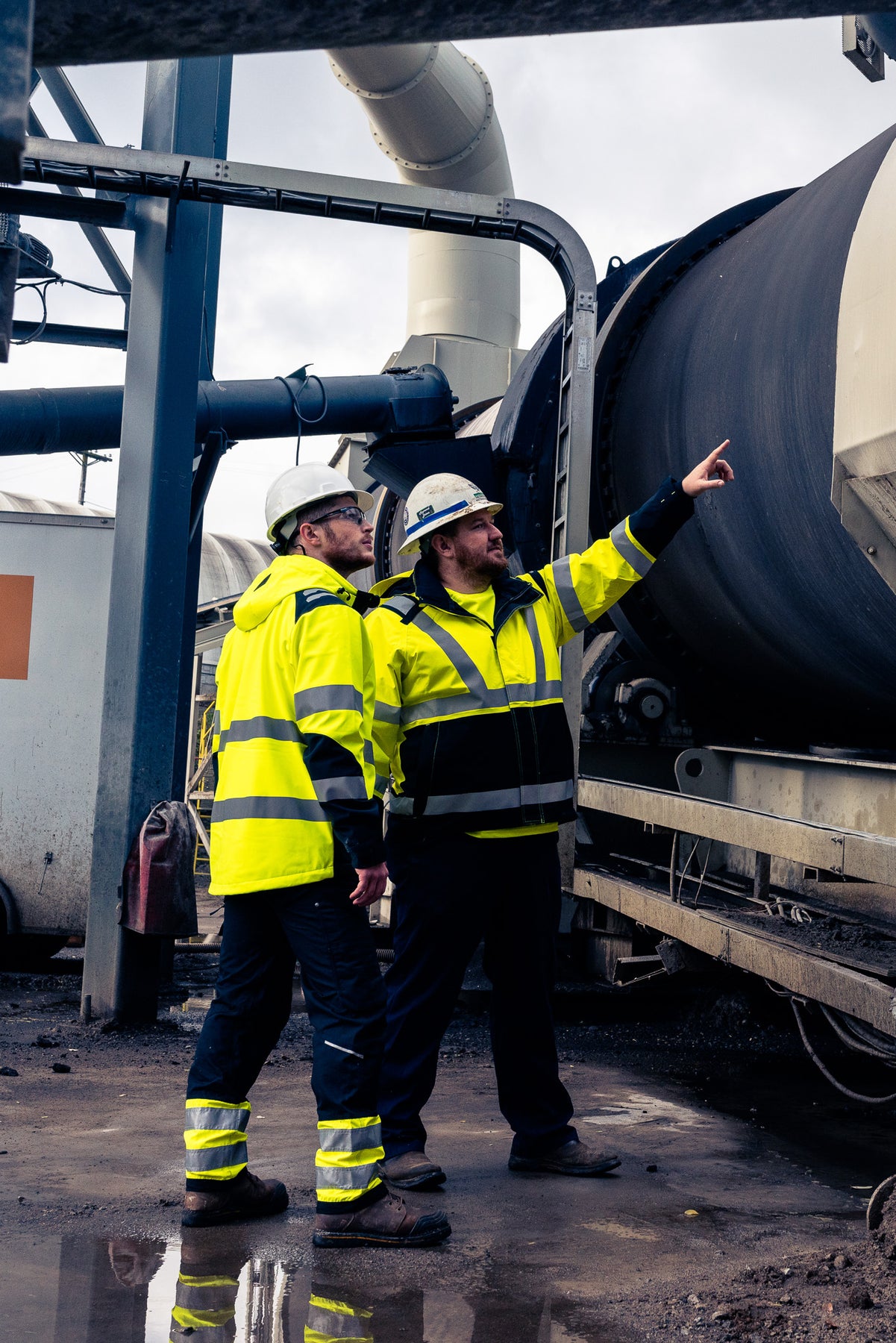 Two workers in high-visibility safety gear inspecting industrial equipment.